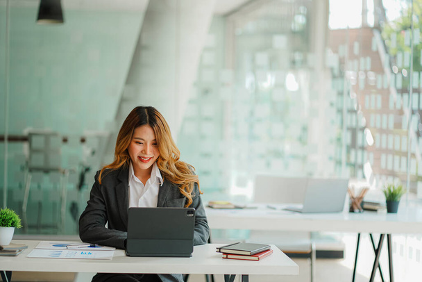 Een Aziatische vrouwelijke accountant zit aan een bureau met een laptop en berekent financiële grafieken met investeringsresultaten. Plan een succesvol bedrijfsgroeiproces op kantoor. - Foto, afbeelding