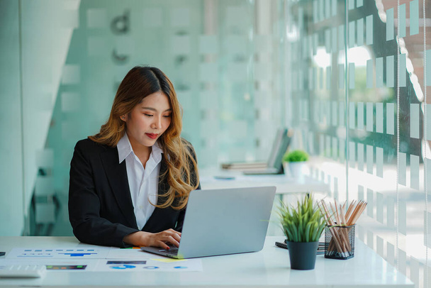 An Asian female accountant sits at a desk with a laptop and calculates financial graphs showing investment results. Plan a successful business growth process in the office. - Photo, image