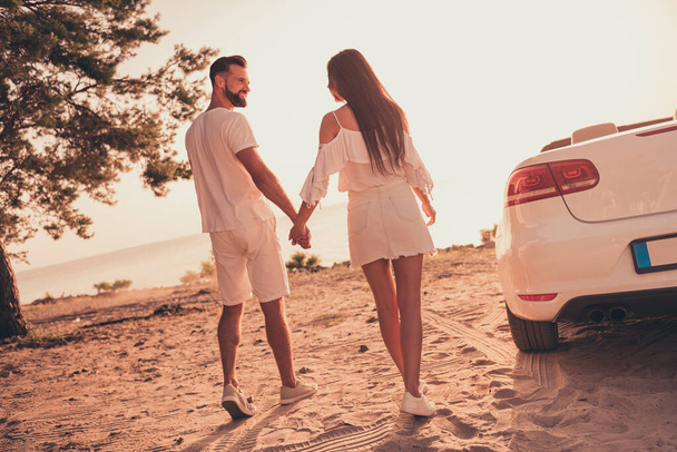 Back rear view full size photo of husband wife hold hands walk beach support romance cabriolet outdoors - Foto, Bild