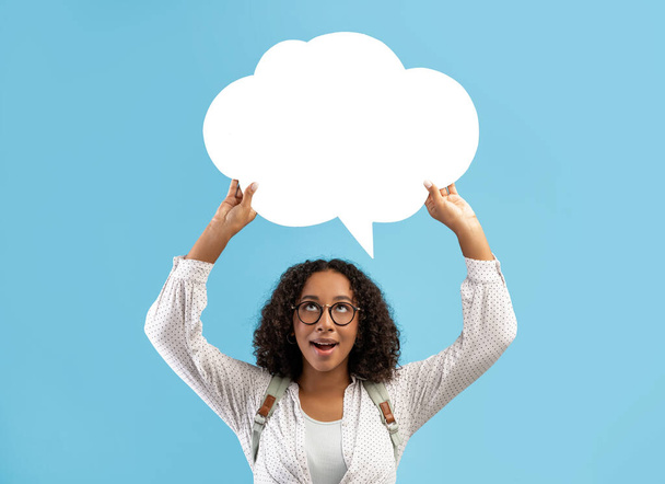Happy black woman holding empty speech bubble above her head, looking up on blue studio background, mockup - Foto, immagini