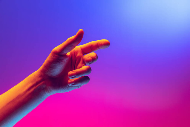 Human hand gesturing isolated on gradient purple-pink background in neon light. Concept of sign language, creativity, symbolism, culture and art - Foto, immagini
