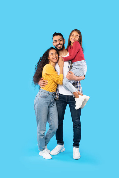 Arabic Man Hugging Wife And Holding Daughter On Blue Background - Фото, изображение