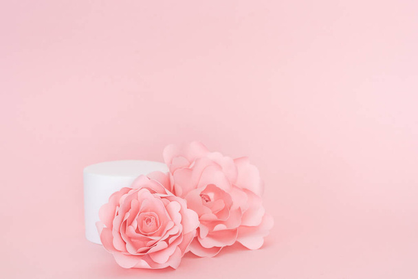 Plataforma circular en blanco para la presentación del producto con rosas de papel sobre fondo rosa. Copiar espacio. - Foto, Imagen