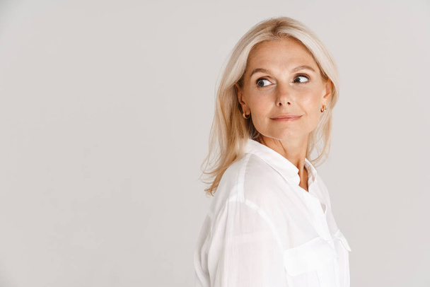 Mature blonde woman wearing shirt posing and looking aside isolated over white background - Fotoğraf, Görsel