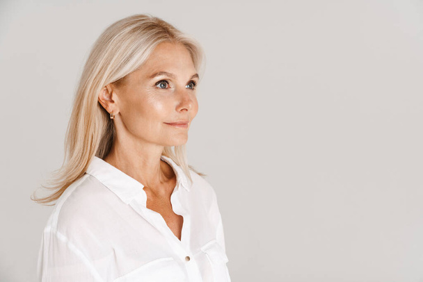 Mature blonde woman wearing shirt posing and looking aside isolated over white background - Фото, зображення