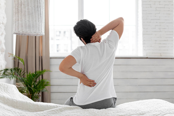 Unrecognizable man suffering from back pain at home in bedroom - 写真・画像