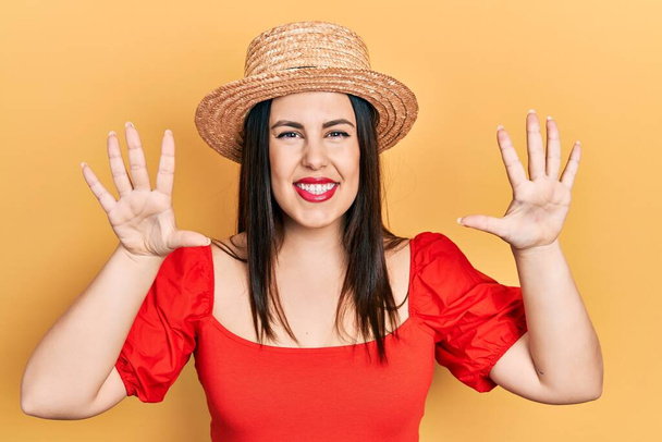 Young hispanic woman wearing summer hat showing and pointing up with fingers number ten while smiling confident and happy.  - Photo, Image