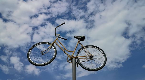 Old bicycle on an iron pole against the blue sky - Zdjęcie, obraz