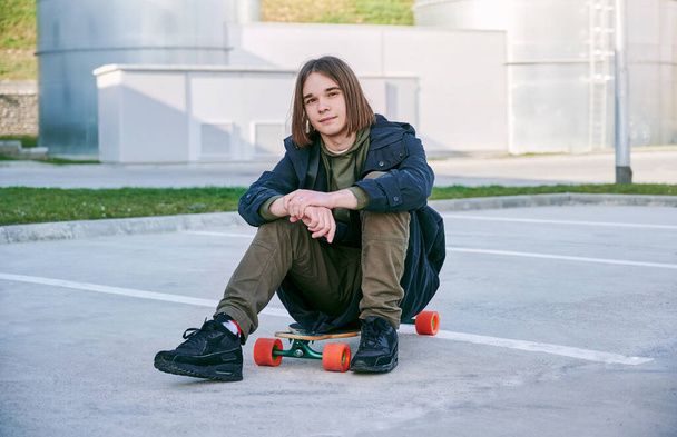 Teenager boy sitting on skateboard outdoor during summer activities. - Foto, afbeelding