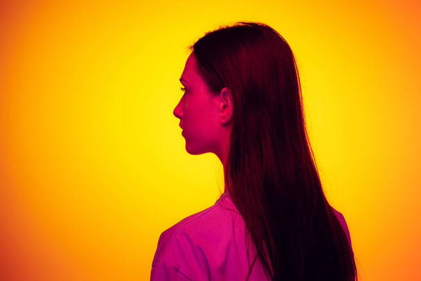 Back view. Portrait of young pretty girl with long shiny hair isolated on yellow color background in neon filter. Concept of emotions, beauty, fashion, youth. - Foto, imagen