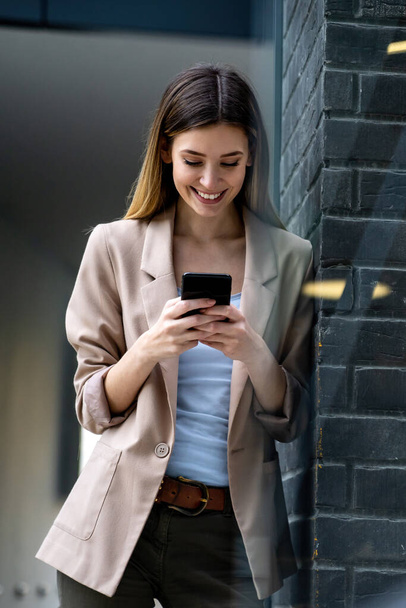Portrait of successful woman with mobile phone in urban background. Business technology device concept - Фото, изображение