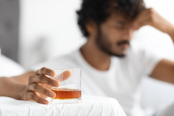 Glas met alcohol in de hand van een donkere man met baard - Foto, afbeelding