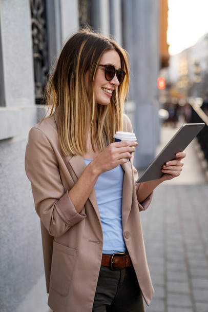 Attractive young successful woman drinking a coffee and using a digital tablet while enjoying break - Foto, Imagem
