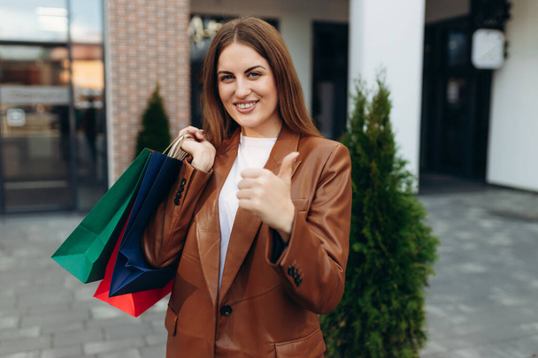 Young costumer woman hold package bags with purchases after shopping show thumb up - Foto, Imagem
