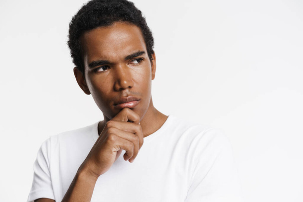 Young black man looking aside while holding his chin isolated over white wall - Fotoğraf, Görsel