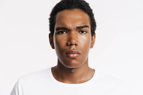 Young black man dressed t-shirt posing and looking at camera isolated over white wall - Foto, Imagen