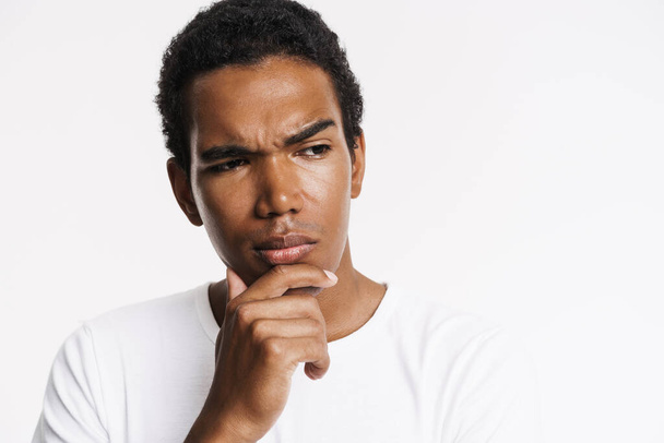 Young black man looking aside and frowning while holding his chin isolated over white wall - Photo, image