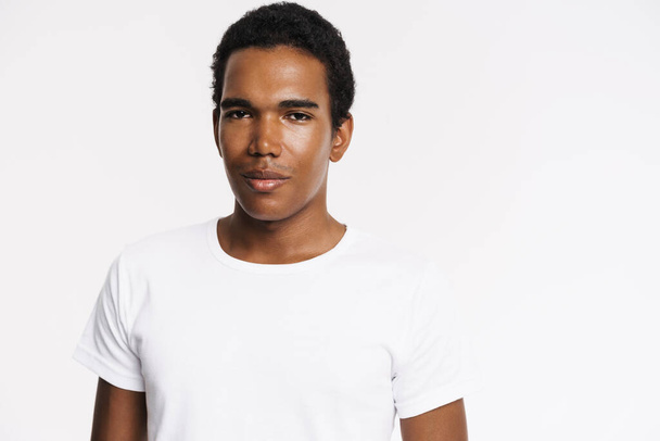 Young black man dressed t-shirt posing and looking at camera isolated over white wall - Foto, Imagem