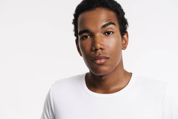 Young black man dressed t-shirt posing and looking at camera isolated over white wall - Foto, imagen