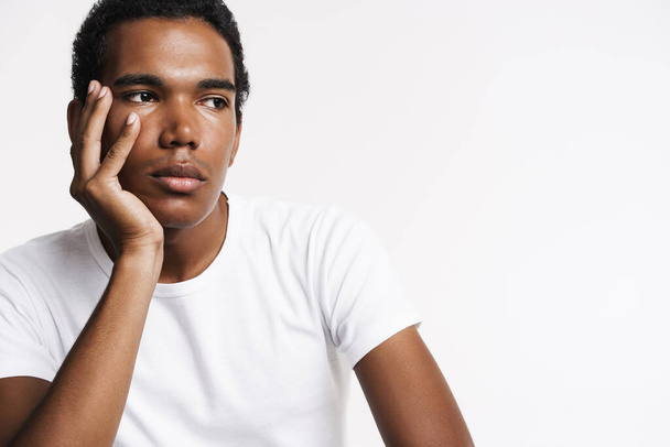 Young black man dressed t-shirt posing and looking aside isolated over white wall - 写真・画像