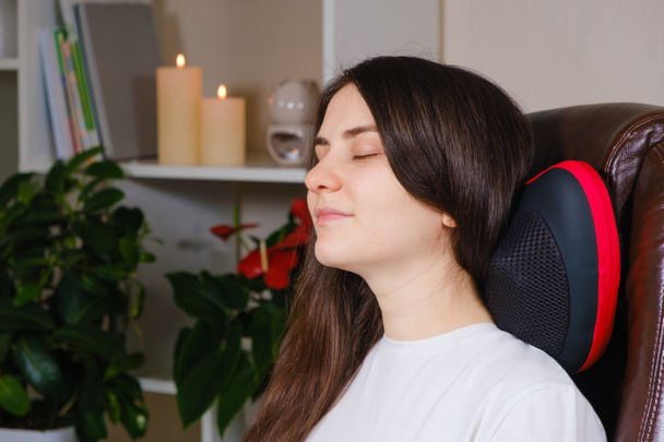Une femme s'assoit sur une chaise avec un oreiller de massage et fait un massage du cou. - Photo, image