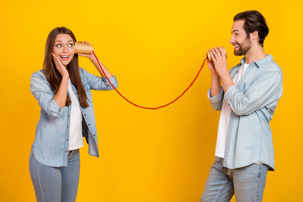 Portrait of two attractive cheerful people using rope phone telling secret isolated over bright yellow color background - Photo, image