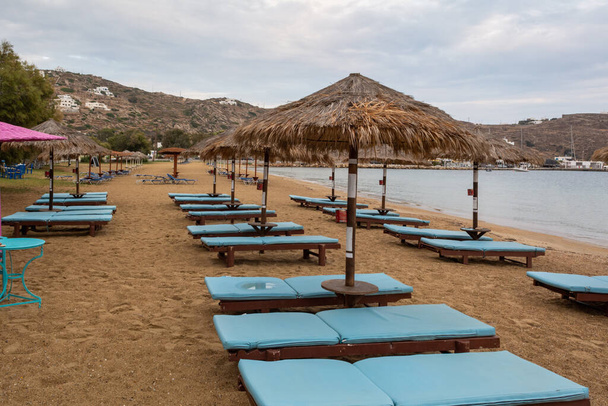 Leżaki plażowe z parasolami na piaszczystej plaży Chora na wyspie Ios. Cyklady, Grecja - Zdjęcie, obraz