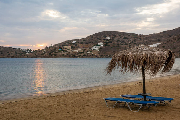 Rieten parasol met ligstoelen op het zandstrand van Chora op het eiland Ios. Cycladen, Griekenland - Foto, afbeelding