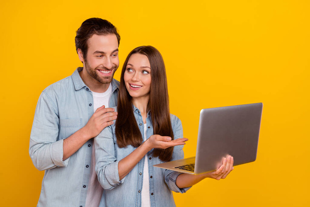 Portrait of handsome beautiful cheery couple using laptop showing ecommerce isolated over bright yellow color background - Foto, afbeelding