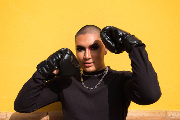 Young non-binary person wears boxing gloves on a mustard yellow background, the person is make up and does different boxing poses. Concept equality, homosexuality, gay, lesbian, gay pride. - Zdjęcie, obraz