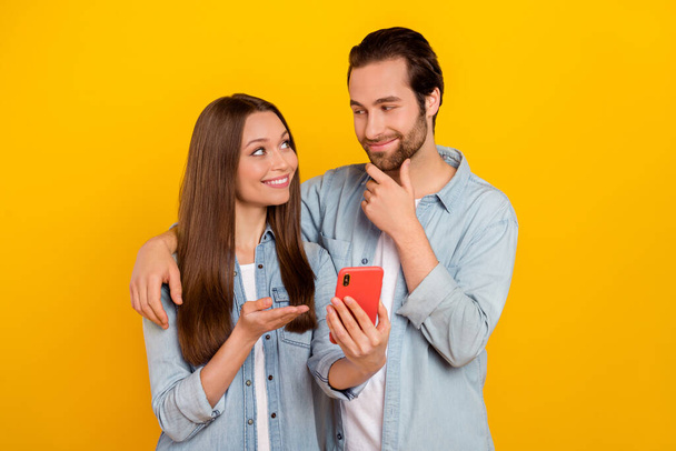 Photo of impressed young brown hairdo couple look telephone wear jeans shirt isolated on yellow background - Φωτογραφία, εικόνα