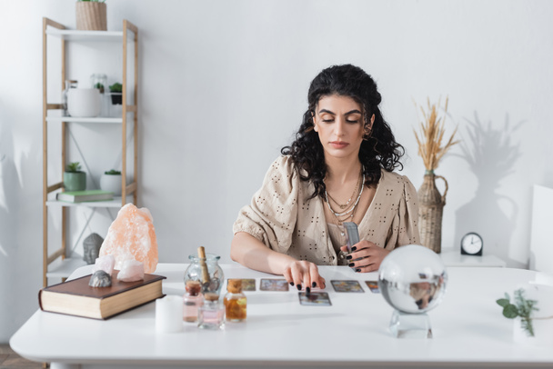 Gypsy fortune teller holding tarot cards near blurred orb on table  - 写真・画像
