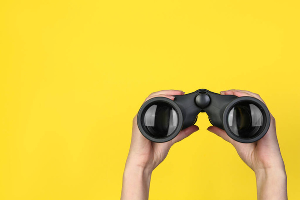 Woman holding modern binoculars on yellow background, closeup. Space for text - Photo, Image