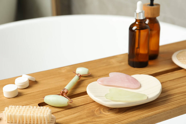Jade and rose quartz gua sha tools, natural face roller with cosmetic products on wooden caddy in bathroom - Zdjęcie, obraz