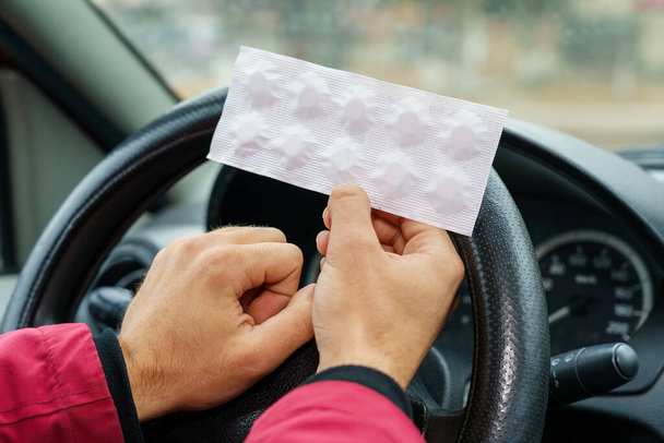 Paczka tabletek w rękach kierowcy na rozmytym tle kierownicy w samochodzie. Stosowanie leków farmakologicznych do celów medycznych podczas prowadzenia pojazdów. Skupienie selektywne - Zdjęcie, obraz
