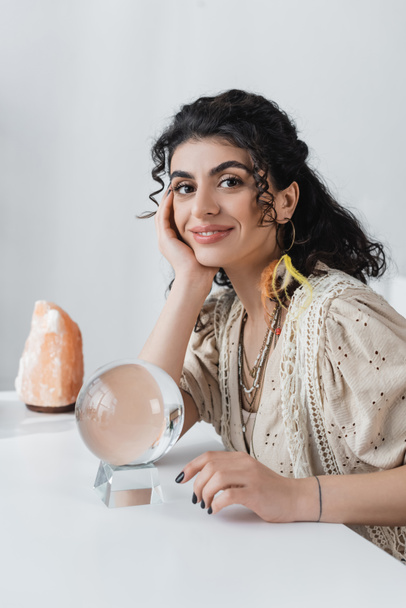 Smiling gypsy fortune teller looking at camera near orb and crystal on table  - Fotografie, Obrázek