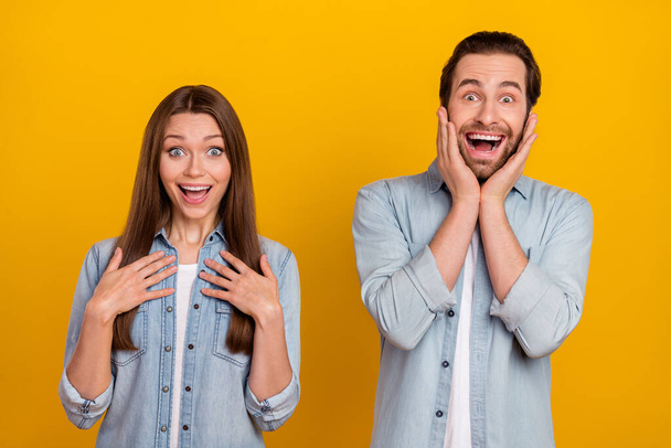 Photo of shocked excited sister brother dressed denim shirts hands arms cheeks chest isolated yellow color background - Zdjęcie, obraz