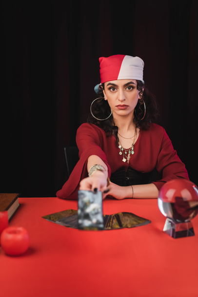Gypsy fortune teller holding blurred tarot and looking at camera isolated on black  - Fotoğraf, Görsel