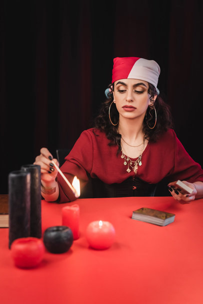 Gypsy soothsayer burring blurred candles and holding tarot isolated on black  - Photo, Image