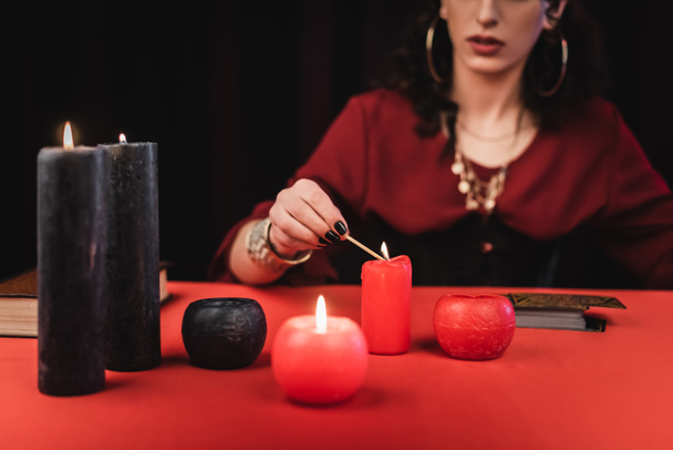 Cropped view of blurred soothsayer burning candles near book and tarot isolated on black  - Foto, Bild