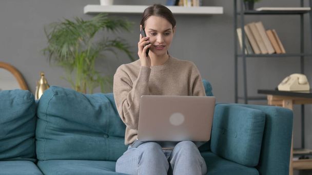 Woman with Laptop Talking on Phone on Sofa  - Foto, imagen