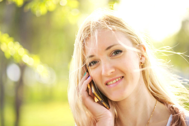 Portret van een mooie jonge vrouw in het voorjaarspark. meisje praten aan de telefoon - Foto, afbeelding