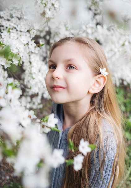 Cute child with blond hair in a blooming garden - Foto, afbeelding
