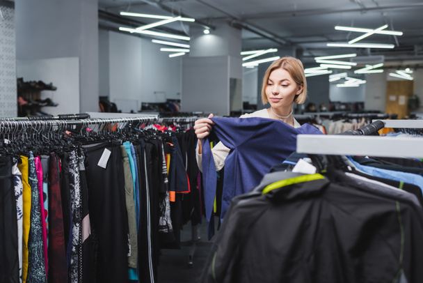Pretty woman choosing clothes in second hand - Фото, изображение