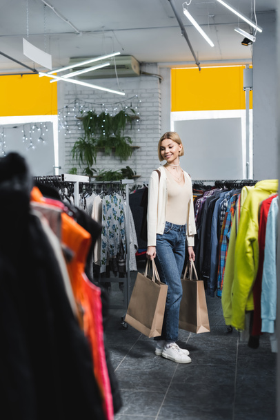 Cheerful woman holding purchases near clothes in second hand  - Foto, Imagem