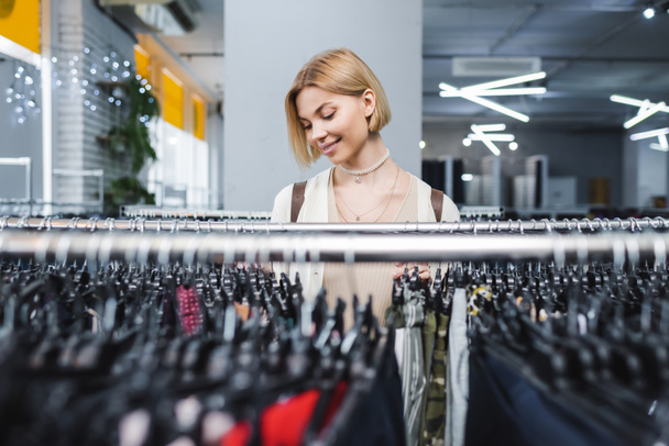 Positive woman choosing clothes in retro store  - Фото, изображение