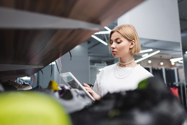 Blonde saleswoman using digital tablet near blurred shelf in second hand  - Foto, immagini