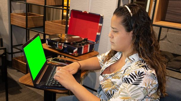 jeune femme assise devant l'ordinateur à côté de la plaque tournante avec disque vinyle, écran vert sur ordinateur portable - Photo, image