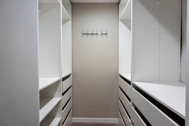 Vista di alti armadi bianchi e cassetti all'interno di una stretta cabina armadio all'interno di una camera matrimoniale - Foto, immagini