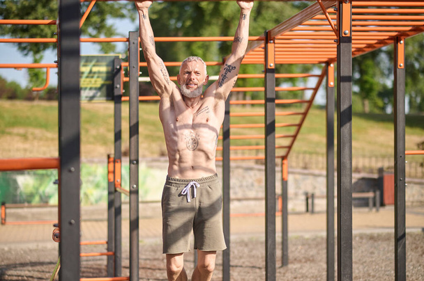 Šedovlasý dospělý muž, který cvičí na otevřeném sportovním hřišti - Fotografie, Obrázek
